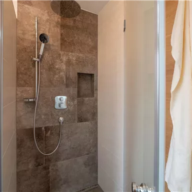 Eine moderne Dusche mit braunen Fliesen und einer klaren Duschwand. Handtücher hängen an der Wand, und die Dusche wirkt einladend.