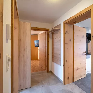 Ein heller Flur mit Holz-Türen und einem modernen Design. Die Wände sind schlicht und die Bodenfliesen sind in neutralen Farben gehalten.