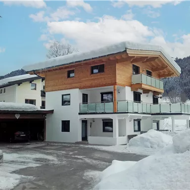 Ein modernes Haus in den Bergen, umgeben von Schnee. Der Himmel ist blau mit einigen Wolken.