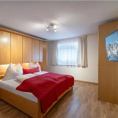 Ein gemütliches Schlafzimmer mit einem großen Bett und Holzschränken. Der Raum hat ein Fenster mit Vorhängen und einen Fernseher an der Wand.