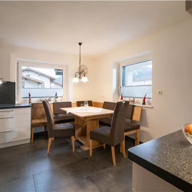 Eine moderne Küche mit einem Essbereich. Der Tisch ist für vier Personen gedeckt und es gibt große Fenster mit Blick nach draußen.