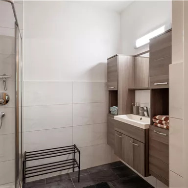 Ein modernes Badezimmer mit einer Dusche und Holzschränken. Die Wände sind hell gefliest und ein Handtuchhalter befindet sich an der Wand.