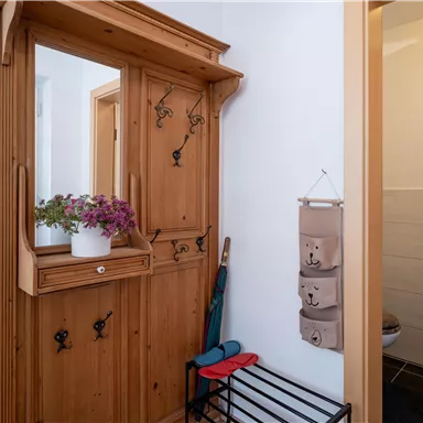Ein einladender Flur mit einem Holzschrank und einem kleinen Spiegel. Neben dem Schrank stehen farbige Regenschirme und ein dekorativer Aufbewahrungshalter.