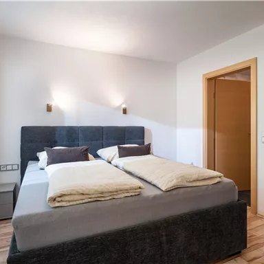 Ein gemütliches Schlafzimmer mit einem Doppelbett und weichen Bettwaren. Es gibt helle Wände und einen großen Spiegel, der den Raum zusätzlich beleuchtet.