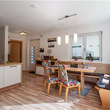 Eine moderne Küche mit einem Esstisch und bunten Stühlen. Viel Licht strömt durch die Fenster, und das Holzdesign sorgt für eine einladende Atmosphäre.