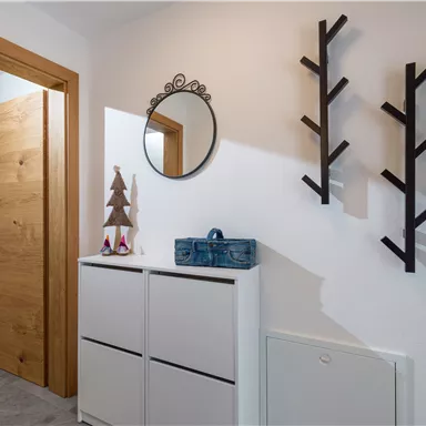 Ein heller Eingangsbereich mit einer Holz-Tür. An der Wand hängen ein Spiegel und dekorative Äste, daneben steht ein Aufbewahrungsschrank.