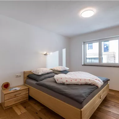 Ein gemütliches Schlafzimmer mit einem Doppelbett und modernen Holzmöbeln. Der Raum hat große Fenster, die viel Licht hereinlassen.