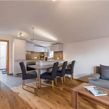 Eine moderne Wohnung mit einem offenen Wohn- und Essbereich. Es gibt eine helle Küchenzeile und einen gemütlichen Sitzbereich.