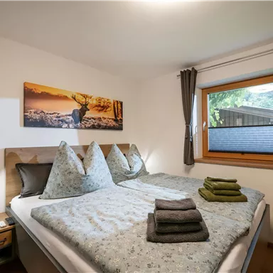 Ein gemütliches Schlafzimmer mit einem Doppelbett und auffälligen Kopfkissen. Große Fenster sorgen für viel Tageslicht und eine angenehme Atmosphäre.
