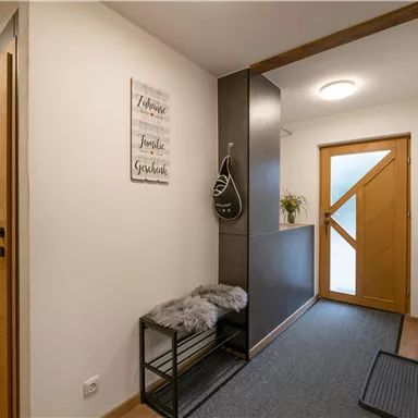 Ein moderner Flur mit Holztüren und einer hellen Eingangstür. Ein kleiner Tisch mit einer Decke und einer Pflanze sorgt für eine einladende Atmosphäre.
