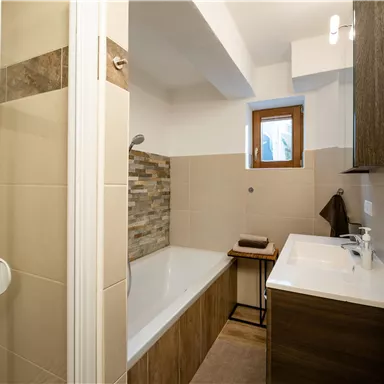 Ein modernes Badezimmer mit einer Dusche und einer Badewanne. Es hat elegante Fliesen und Holzlemente für einen warmen, einladenden Look.