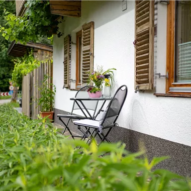 Ein gemütlicher Balkon mit einem kleinen Tisch und Stühlen. Umgeben von grünen Pflanzen und einem malerischen Blick auf die Straße.
