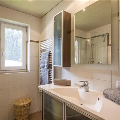 Ein modernes Bad mit einer großen Dusche und einem Fenster, das Tageslicht hereinlässt. Die Wände sind hell gefliest und es gibt frische Handtücher sowie einen Wäschekorb.