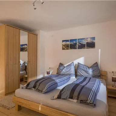 Ein gemütliches Schlafzimmer mit einem großen Bett und blauen Bettwäsche. Der Raum ist hell und modern, mit einem Kleiderschrank und Bildern an der Wand.