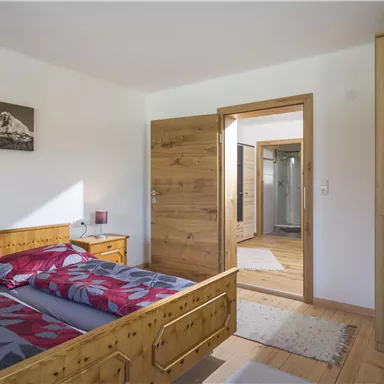 Ein gemütliches Schlafzimmer mit einem Doppelbett und Holzdetails. Der Raum hat eine helle, einladende Atmosphäre und einen Blick auf ein Badezimmer.