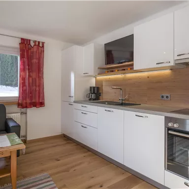 Eine moderne Küche mit weißen Möbeln und Holzdetails. Es gibt Fenster mit roten Vorhängen und einen gemütlichen Sitzbereich.
