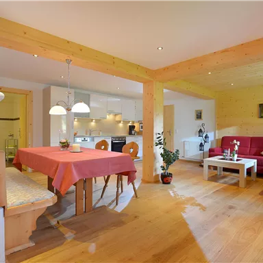 A cozy living space with a dining table and a red couch. The room has wooden floors and plenty of natural light.