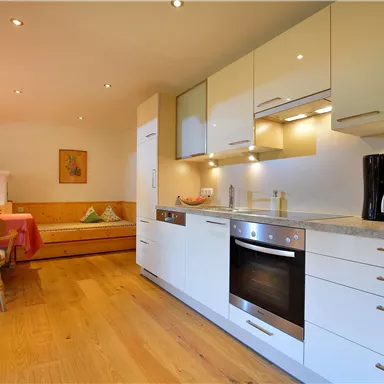 A modern kitchen with light cabinets and a stone countertop. In the background, there is a cozy dining area with a table and chairs.