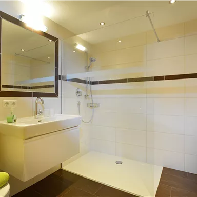 A modern bathroom with a large shower and an elegant sink. The walls are tiled in light colors, and fresh towels are laid out.