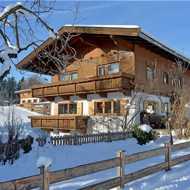 A cozy wooden house in the snow, surrounded by trees. The balconies are beautifully decorated, and the surroundings are wintery and tranquil.