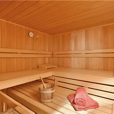A cozy sauna with wooden paneling and a small bucket. A red towel is lying on one of the benches.