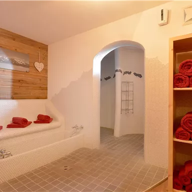 A cozy wellness area with a white bathtub and red towels. Wooden elements and a tasteful picture can be seen on the wall.