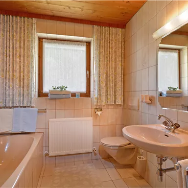 Ein modernes Badezimmer mit einer Dusche, Badewanne und einem Waschbecken. Die Wände sind gefliest und es gibt Holzdetails sowie Fenster mit Vorhängen.