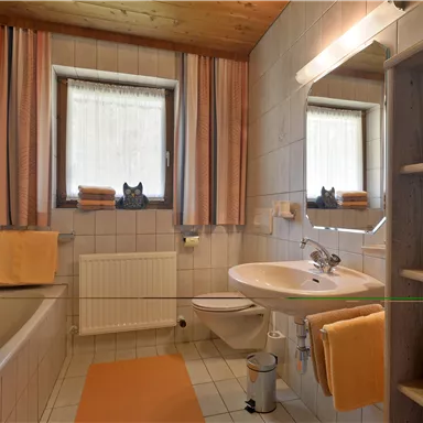 Ein modernes Badezimmer mit einer Badewanne und einem Waschbecken. Es sind beige und orangefarbene Handtücher sowie eine Holzdecke sichtbar.