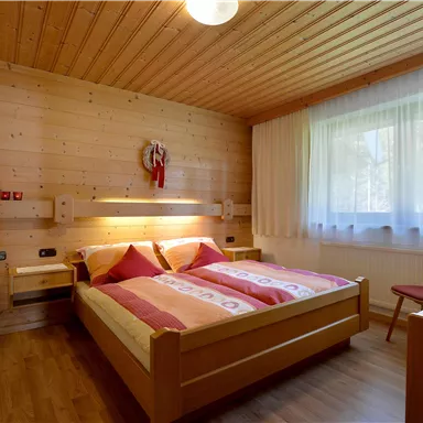 Ein gemütliches Zimmer mit Holzverkleidung und zwei Betten. Der Raum ist hell und freundlich mit großen Fenstern und einer kleinen Sitzecke.