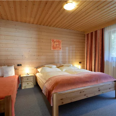 Ein gemütliches Schlafzimmer mit Holzverkleidung und großen Fenstern. Es gibt ein Doppelbett und ein Einzelbett, in warmen Farben dekoriert.