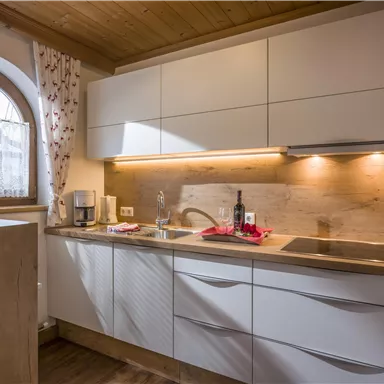 Eine moderne Küche mit weißen Schränken und Holzdetails. Heller Raum mit natürlichem Licht durch ein rundes Fenster.