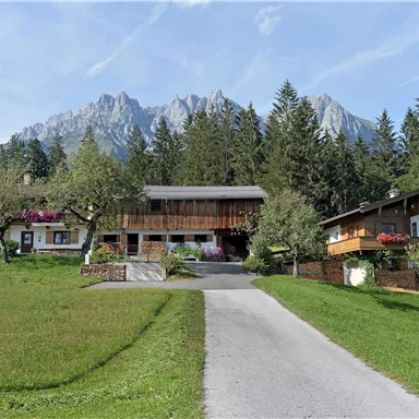 Eine malerische Landschaft mit traditionellen Chalets und grünen Wiesen. Im Hintergrund erheben sich majestätische Berge unter einem klaren Himmel.