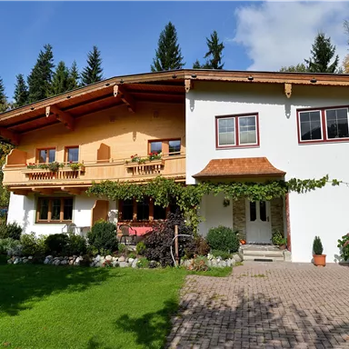 A beautiful, traditional house with a wooden balcony and blooming plants. The garden is well-tended and surrounded by trees.