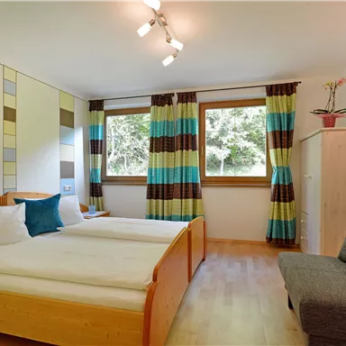 A cozy bedroom with two beds and modern furniture. Large windows provide plenty of daylight and a pleasant atmosphere.
