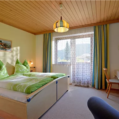 A cozy bedroom with two beds and colorful cushions. The room has a large window with a beautiful view and a television.