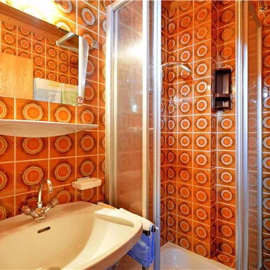 A small bathroom with a shower cabin and modern equipment. The walls are decorated with orange tiles.