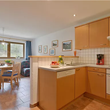 A modern kitchen with wooden cabinets and a cozy dining area. Plenty of light streams through the windows, creating an inviting atmosphere.