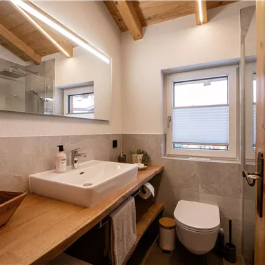 A modern bathroom with wood details and an elegant washbasin. Bright walls and a window provide plenty of daylight.