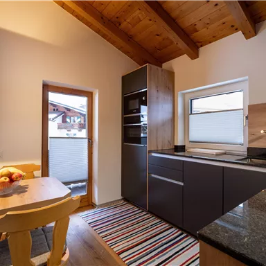 A modern kitchen with wooden ceilings and elegant furniture. Fresh fruits are on the table, and the room is bright and inviting.