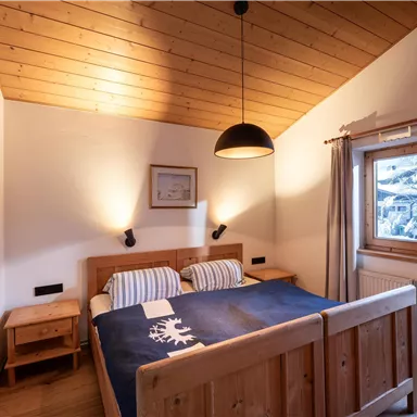 A cozy bedroom with wooden walls and a four-poster bed. Large windows provide plenty of daylight and a view outside.