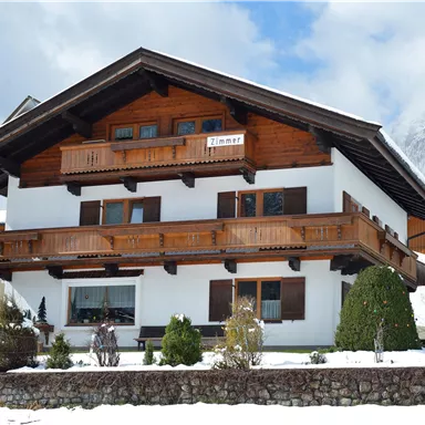 A beautiful alpine house with wooden balconies. Snow covers the garden and the surroundings.