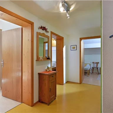 A bright hallway with wooden details and several doors. A small dresser and a mirror complement the decor.