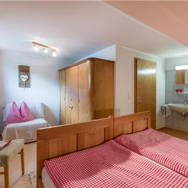A cozy bedroom with two single beds, a wooden wardrobe, and a small sink. The walls are light and the room is well-lit.