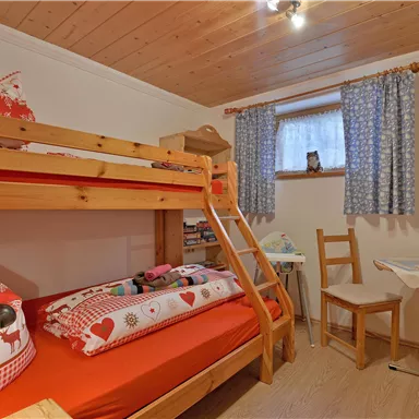 Ein gemütliches Schlafzimmer mit einem Etagenbett und bunten Kissen.
Etagenbett untere Ebene ca. 1,20 m breit, obere Ebene ca. 90 cm breit.
Ein kleiner Tisch und ein Stuhl ergänzen den Raum, der von natürlichem Licht durch ein Fenster erhellt wird.