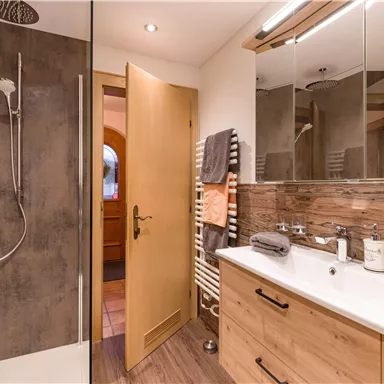 Ein modernes Badezimmer mit einer Dusche und Holzverkleidung. Der Raum ist hell und gut organisiert mit Handtüchern und Pflegeprodukten.