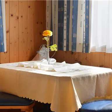 A cozy table with a white tablecloth in a wooden room. In the center stands a blooming flower in a vase.