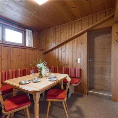 A cozy room with wooden walls and red upholstery. A dining table is set and a staircase leads to another area.