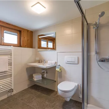 A modern bathroom with a shower, toilet, and a large mirror. Bright tiles and wood elements create an inviting atmosphere.