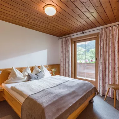 A cozy bedroom with a wooden ceiling and a large bed.
Large windows offer a view of nature outside.