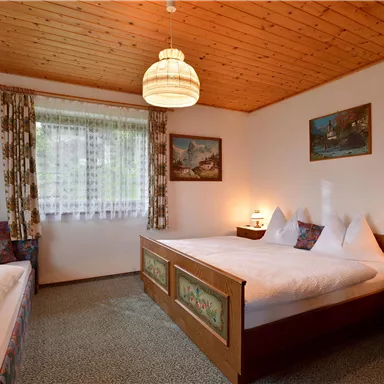 A cozy bedroom with two beds and a wooden ceiling. Soft lighting and decorative elements give the room an inviting atmosphere.